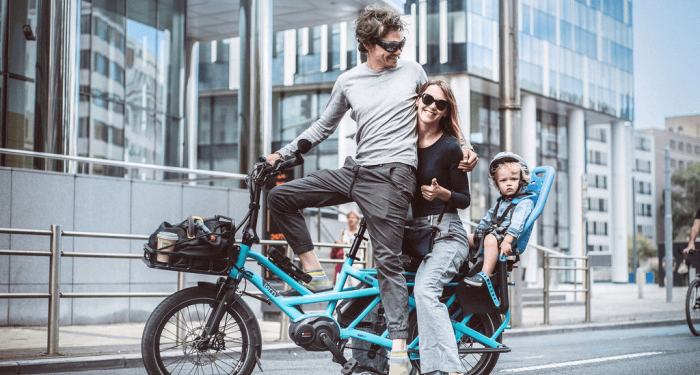 Vader en moeder omhelzen elkaar op de fiets terwijl hun kind achterop zit